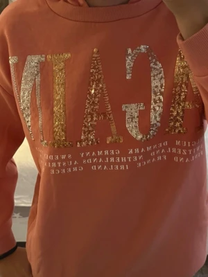 Jättefin aprikos/korallfärgad hoodie från Name It - Säljer denna jättefina hoodie från Name It som är aprikos/korallfärgad och det står ”AGAIN” och olika länder. Den är inte använd många gånger så jättebra skick. Den är i stl 158-164, men är lite kort i ärmarna på mig som är 172 cm lång. Hör av er om frågor!💗