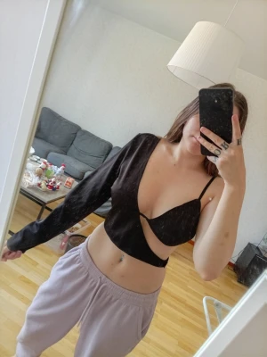 Svart croppad oneshoulder topp - Trendig svart croppad topp med unik oneshoulder-design. Ena sidan har lång ärm medan den andra är axelbandslös, vilket ger en edgy och modern look. Perfekt för dig som vill sticka ut och gillar statement-plagg.