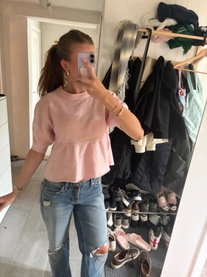 Ljusrosa stickad topp med volang - Supersöt ljusrosa stickad topp med volang nedtill och halvlånga ärmar. Tröjan har rund halsringning och en avslappnad passform som ger en gullig och trendig look. Perfekt att styla med jeans eller kjol för en casual vibe.