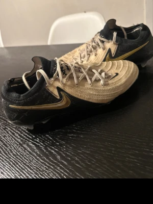 Nike Phantom vit/svart/guld fotbollsskor - Säljer ett par Nike Phantom fotbollsskor i svart och guld med snygg design och snörning. Skorna har en lätt ovandel i syntetmaterial och är perfekta för dig som vill ha bra grepp och kontroll på planen. Guldiga detaljer och klassisk Nike-logga på sidan.