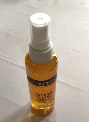 Neutrogena Clear & Soothe Toning Mist - Fräsch ansiktsmist från Neutrogena i en genomskinlig plastflaska med sprayfunktion. Innehållet är gult och formulan är oljefri, berikad med gurkmeja för att lugna och återfukta huden. Passar både normal och känslig hy.