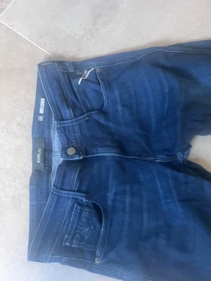 Replay Anbass blå jeans  - Säljer ett par Replay Anbass jeans i ljusblå tvätt med slitna detaljer och skinny passform. Jeansen har klassisk femficksdesign, läderpatch bak. Perfekt för dig som gillar en modern och avslappnad stil. Sitter som 30.32 