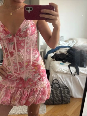 Rosa mönstrad miniklänning med volang - Supersöt miniklänning i rosa och vitt med spetsdetaljer, tunna axelband och volang nedtill. Aldrig använd 