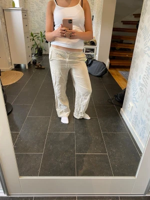 Beiga linnebyxor med dragsko - Säljer ett par beiga linnebyxor med avslappnad passform och dragsko i midjan. Byxorna har raka ben och resår i midjan för extra komfort. Perfekta för en chill och stilren look. Materialet är luftigt linne som passar bra till sommaren.