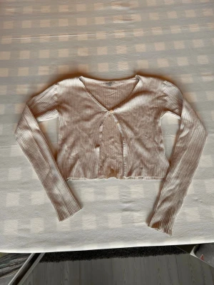 Beige ribbad kofta  - Säljer en beige ribbad kofta med v-ringning och två små knappar framtill. Perfekt att slänga över ett linne eller t-shirt för en chill look.