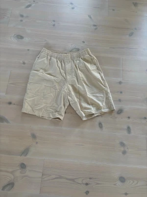 Beige linneshorts Uniqlo - Säljer ett par beige shorts med avslappnad passform och elastisk midja. Shortsen har sidofickor och är tillverkade i ett mjukt bomullsliknande material. Perfekta för varma dagar och enkel stil.
