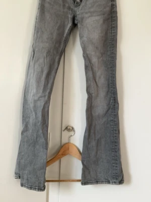 Grå bootcut jeans från Gina Tricot - Snygga grå bootcut jeans från Gina Tricot i storlek 158. Jeansen har knäppning med tre silverfärgade knappar och klassisk femficksdesign. Perfekta för dig som gillar en avslappnad men trendig look.