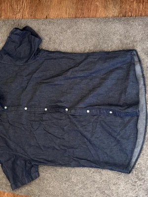 Mörkblå skjorta från Jack & Jones - Snygg mörkblå skjorta från Jack & Jones i bomull. Skjortan har korta ärmar, klassisk krage och knappar längs hela framsidan. Perfekt till jeans eller chinos för en clean och enkel stil.