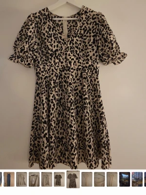 Leopardmönstrad klänning med puffärm - Kort klänning med leopardmönster i beige och svart. Modellen har puffiga korta ärmar med volangkant och rund halsringning med liten öppning fram. Kjolen är lätt utställd för en flowy känsla. Passar xs-s 