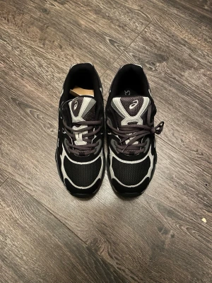 Svarta Asics - HELT NYA UTAN SKO KARTONG……Snygga sneakers från Asics i svart och grått med vita detaljer. Skorna har meshpaneler för bra ventilation och klassisk snörning. Yttersulan är robust och designen är sportig med retrovibbar. Perfekta för dig som gillar streetwear och sportig stil.   