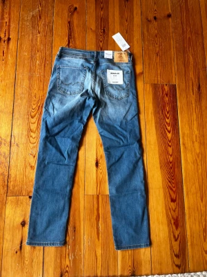 Jack & Jones ljusblå regular jeans - Säljer ett par ljusblå jeans från Jack & Jones i modellen Clark. Jeansen har regular fit, normalhög midja och raka ben. Klassisk femficksmodell med snygga slitningar och patch i läderimitation bak. Perfekta för en avslappnad stil.