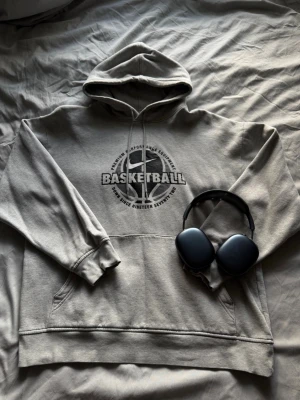 Vintage Nike hoodie  - Snygg grå hoodie från Nike med stort basketboll-tryck och texten 'Basketball' på bröstet. Klassisk känguruficka, huva med dragsko och ribbade muddar. Perfekt för dig som gillar sportig streetstyle och vill ha en bekväm och stilren look.
