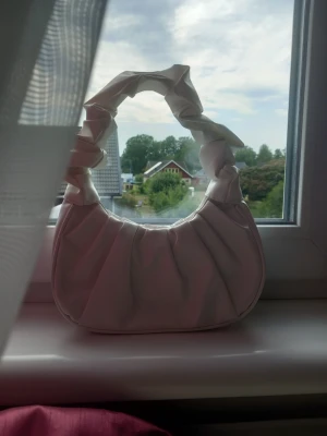 Vit väska - Vit handväska i konstläder med rynkad axelrem och rundad form. Väskan har magnetlås. Perfekt för lite småsaker när man ska till exempel till stan med sina vänner eller ut och shoppa❣️