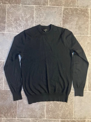 Svart stickad tröja med rund hals - En klassisk svart stickad tröja med rund halsringning och långa ärmar. Tröjan har ribbade muddar vid ärmslut och nederkant, vilket ger en snygg och enkel look. Perfekt att matcha med jeans eller kjol för en stilren outfit.