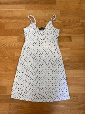 Vit blommig sommarklänning Primark - Söt vit klänning från Primark med små blå blommor och smala axelband. Klänningen har knappar framtill och är i ett mjukt, ribbat bomullstyg. Perfekt för varma dagar och har en avslappnad passform.