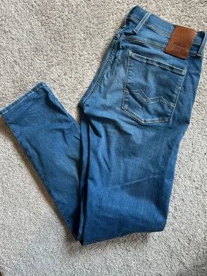 Replay anbass hyperflex - Säljer ett par blå replay anbass hyperflex med snygga slitningar och tvättade detaljer på framsidan och baksidan. Jeansen är i storlek 32 och är slim fit. Jeansen har ett litet hål i vänsterfickan, se bild 6.