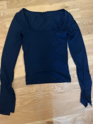 Mörkblå långärmad topp Gina Tricot - Snygg mörkblå långärmad topp från Gina Tricot med bred, rundad urringning. Tillverkad i mjukt och stretchigt material som sitter tight mot kroppen. Perfekt att styla med jeans eller kjol för en trendig look.