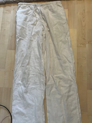 Vita linnebyxor - Säljer ett par vita linnebyxor med avslappnad passform. Byxorna har raka ben och är tillverkade i ett lätt och luftigt linnetyg, perfekta för en chill och stilren look. Inga synliga fickor eller detaljer.