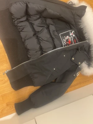 Svart dunjacka med pälskrage - Snygg svart dunjacka med stor vit pälskant på huvan och ribbade muddar. Använd bara i 2 månader i storlek XS perfekt för dig som vill ha en varm och skön jacka in för vintern. Pris kan diskuteras.