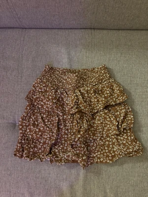 Brun blommig volangkjol - Brun kjol med små vita blommor och volangdetaljer.