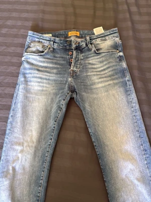 Ljusblå slitna jeans med knappar - Säljer ett par ljusblå jeans med slitningar och snygg tvätt. Jeansen har knappgylf, fem fickor och slim passform. Storlek 31/30. Säljer eftersom dom inte riktigt passade mig, hör av er om fler bilder! :)