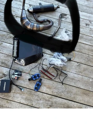 Mopeddelar och trimdelar mix - Säljer ett paket med olika mopeddelar, bland annat avgassystem från Leovince, blåa aluminiumdelar, kåpa med LED-ljus, kablar och elektronik. Perfekt för dig som vill trimma eller laga din moped. Allt på bilden ingår.