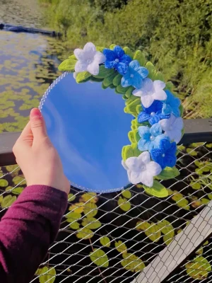 Rund spegel med blå blommor - En rund spegel dekorerad med handgjorda blommor i blått, vitt och grönt. Spegelns kant är prydd med små pärlor och blommorna ger en unik och kreativ look. Perfekt för att piffa upp sminkhörnan och ge en personlig touch till rummet. Kan också vara den perfekta presenten för någon du tycker om!