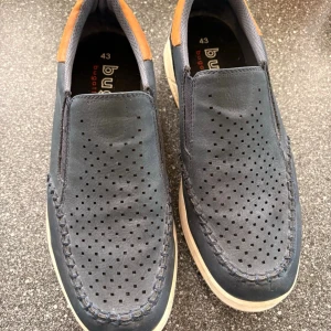 Mørkeblå loafers från Bugatti - Snygga mørkeblå loafers från Bugatti i läder med perforerat mönster på ovandelen och kontrastdetaljer i brunt vid hälen. Skorna har vita sulor och elastiska partier på sidorna för enkel påtagning. Perfekta för en avslappnad men stilren look.