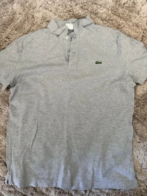 Grå piké från Lacoste slim fit - Säljer en stilren grå pikétröja från Lacoste i slim fit-modell. Hittade den i garderoben nu när jag ska flytta och passar inte i den längre