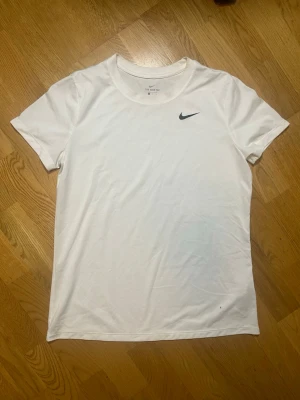 Vit Nike t-shirt med logga - Säljer denna klassiska vita t-shirt från Nike i storlek M (kan passa även S) med svart Nike-logga på bröstet. Tillverkad i mjuk bomull och har rund halsringning samt korta ärmar. Perfekt för en sportig och clean look. Vid frågor, extra bilder eller liknande är det bara att kontakta mig!