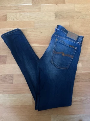 Nudie jeans - Säljer ett par mörkblå jeans från Nudie. Jeansen har fem fickor och en läderpatch bak i midjan. Perfekta för dig som gillar en stilren look. Hör av er vid funderingar! 