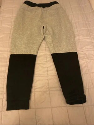 Grå och svarta mjukisbyxor - Säljer ett par mjukisbyxor i grått och svart med bred resår i midjan och muddar vid bensluten. Byxorna har en relaxed fit och är tillverkade i mjukt sweatshirtmaterial, perfekta för chill dagar. Fickor på sidorna för mobilen eller nycklar.