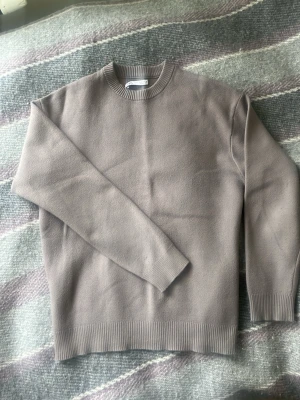 Beige stickad tröja - En stilren beige stickad tröja med rund halsringning och ribbade muddar vid ärmslut och nederkant. Materialet är mjukt och bekvämt ut.      Strl S | passar ca 170