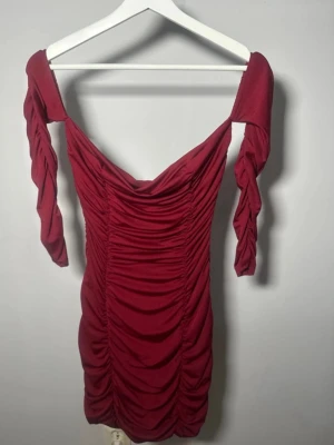 Vinröd off shoulder rynkad miniklänning strl M - Vinröd figurnära off shoulder-klänning från Shein med långa ärmar och rynkad design framtill och baktill. Kort modell med stretchigt material.  Märkt storlek M men är liten i storleken och passar mer som S. Endast provad, aldrig använd.