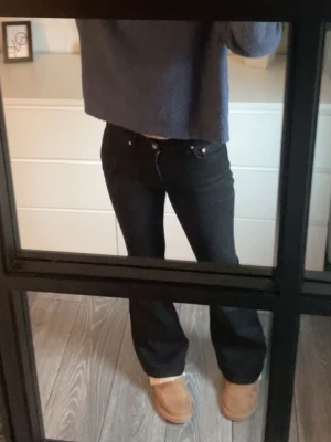 Svarta utsvängda jeans med låg midja - Säljer ett par svarta jeans med utsvängd passform och låg midja. Jeansen har klassiska fem fickor och knappgylf. Perfekta till en avslappnad stil och passar till det mesta i garderoben.