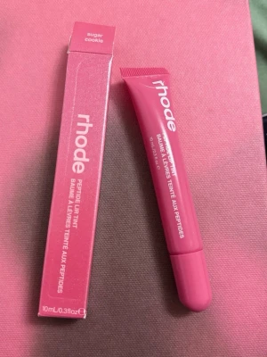 Rhode Peptide Lip Tint Sugar Cookie - Rhode Peptide Lip Tint i färgen Sugar Cookie är ett läppbalsam med peptider som ger återfuktning och en lätt rosa ton. Kommer i en smidig tub med matchande rosa förpackning. Perfekt för dig som vill ha mjuka och snygga läppar.