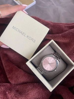Michael Kors klocka med rosa urtavla - Stilren klocka från Michael Kors med silverfärgad länk i rostfritt stål och en snygg rosa urtavla. Klassisk rund form och minimalistisk design som ger en modern vibe. Perfekt accessoar för dig som vill ha något trendigt och elegant.