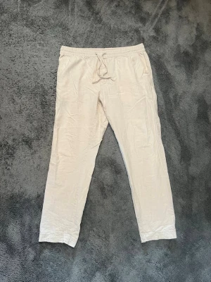 Linnebyxor  - Säljer ett par ljusbeige linnebyxor med avslappnad passform och elastisk midja. Använda men fortfarande i bra skick utöver defekterna vid byxornas nederkant. Hör av dig om du har frågor😇