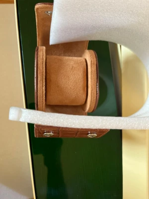 Brun klocklåda i skinnimitation - Snygg och stilren klocklåda i brun skinnimitation med krokodilpräglat mönster. Insidan är klädd i mjukt beige material och har plats för en klocka. Perfekt för att förvara eller resa med din favoritklocka.