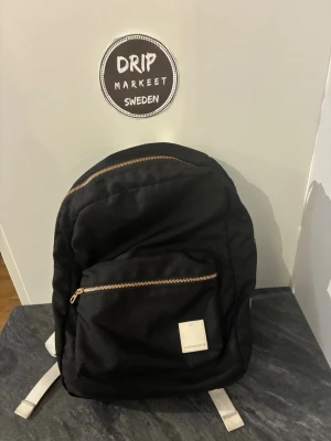 svarg björn borg ryggsäck med vita detaljer - Snygg svart ryggsäck med vita axelband och dragkedjor i metall. Framtill finns en stor ficka med dragkedja och en vit etikett. Perfekt för skola eller cityhäng, rymmer laptop och annat viktigt.