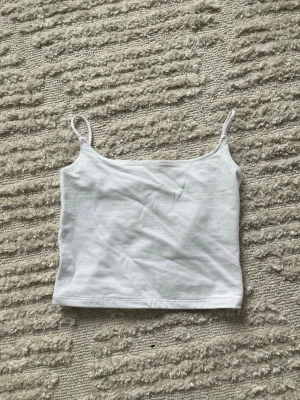 Vit linnetopp från 7B Sister XS - En basic vit linnetopp från 7B Sister i storlek XS. Toppen har smala axelband och är tillverkad i mjuk bomull, perfekt att styla till jeans eller kjol. Enkel och stilren design som funkar till många outfits.