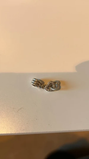  Hjärt berlock från Pandora  - En fin äkta hjärt berlock från Pandora, det överta hjärtat har diamanter och det understa hjärtat blankt silver, jag säljer berlocken för att jag har lite förmåga berlocker och vill bara ha berlocker som inte hänger så mycket.                !OBS! ARMBANDET HÄNGER INTE MED