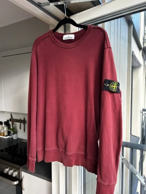 Vinröd sweatshirt från Stone Island - Säljer en vinröd sweatshirt från Stone Island med klassisk patch på vänster ärm. Tröjan har rund halsringning, långa ärmar och ribbade muddar. Perfekt för dig som gillar streetwear och vill ha en stilren look.