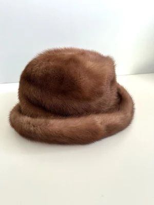 Brun hatt / mössa i 100% äkta päls - storlek 53 /S - Elegant brun pälshatt i 100% äkta päls (mink) i storlek S / 53 cm omkrets. Klassisk design med rund topp, som kan fällas in efter smak. Mjuk och fyllig textur, med en slät insida i matchande färg. Den breda uppvikta kanten ger en sofistikerad silhuett. Passar utmärkt för att komplettera en vintergarderob. Mycket gott skick, som ny!