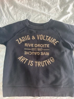 Zadig & Voltaire tröja  - Cool svart sweatshirt från Zadig & Voltaire med beige texttryck framtill där det står 'Art is Truth' och 'Rive Droite'. Tröjan har rund halsringning och långa ärmar. Perfekt för en avslappnad och trendig look.