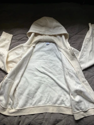 Beige hoodie med dragkedja från Zara - Säljer en beige hoodie från Zara med dragkedja framtill och justerbar huva med snören. Hoodien är tillverkad i mjukt bomullsmaterial och har ribbade muddar vid ärmslut och nederkant. Perfekt för en avslappnad och stilren look.