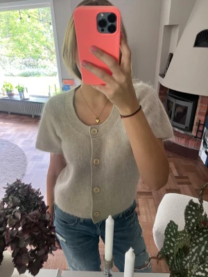 Mohair kofta Cos  - Mysig beige kofta med korta ärmar och stora knappar framtill. Koftan har en rund halsringning och är stickad i ett fluffigt material som ger en soft look. Perfekt att slänga över ett linne eller t-shirt för en avslappnad stil.