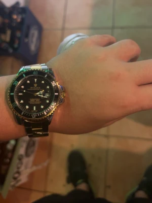  Submariner klocka - Stilren Submariner med svart urtavla och silverfärgad länk i metall. Klockan har tydliga markeringar, datumfönster och vridbar bezel. Perfekt accessoar för dig som gillar klassisk och exklusiv stil.