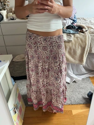 Långkjol med bohemiskt mönster - Lågmidjad långkjol i mjukt, luftigt material med bohemiskt mönster i vinrött, rosa och vitt. Kjolen har bred resår i midjan och volang längst ner. Perfekt för en avslappnad och trendig stil. Passar storlek 34-40 då den är väldigt flowy och stretchig.