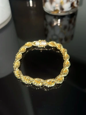 14k guldpläterad cordell armband - Snyggt armband i guldfärgad metall med tvinnad design som ger en chunky och trendig look. Låset är dekorerat med små detaljer för extra bling. Perfekt accessoar för att lyfta din outfit och ge en lyxig känsla.